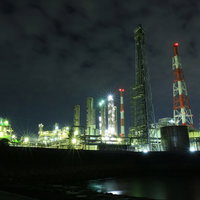 夜間にライトアップされた工場プラントと光芒の夜景の写真