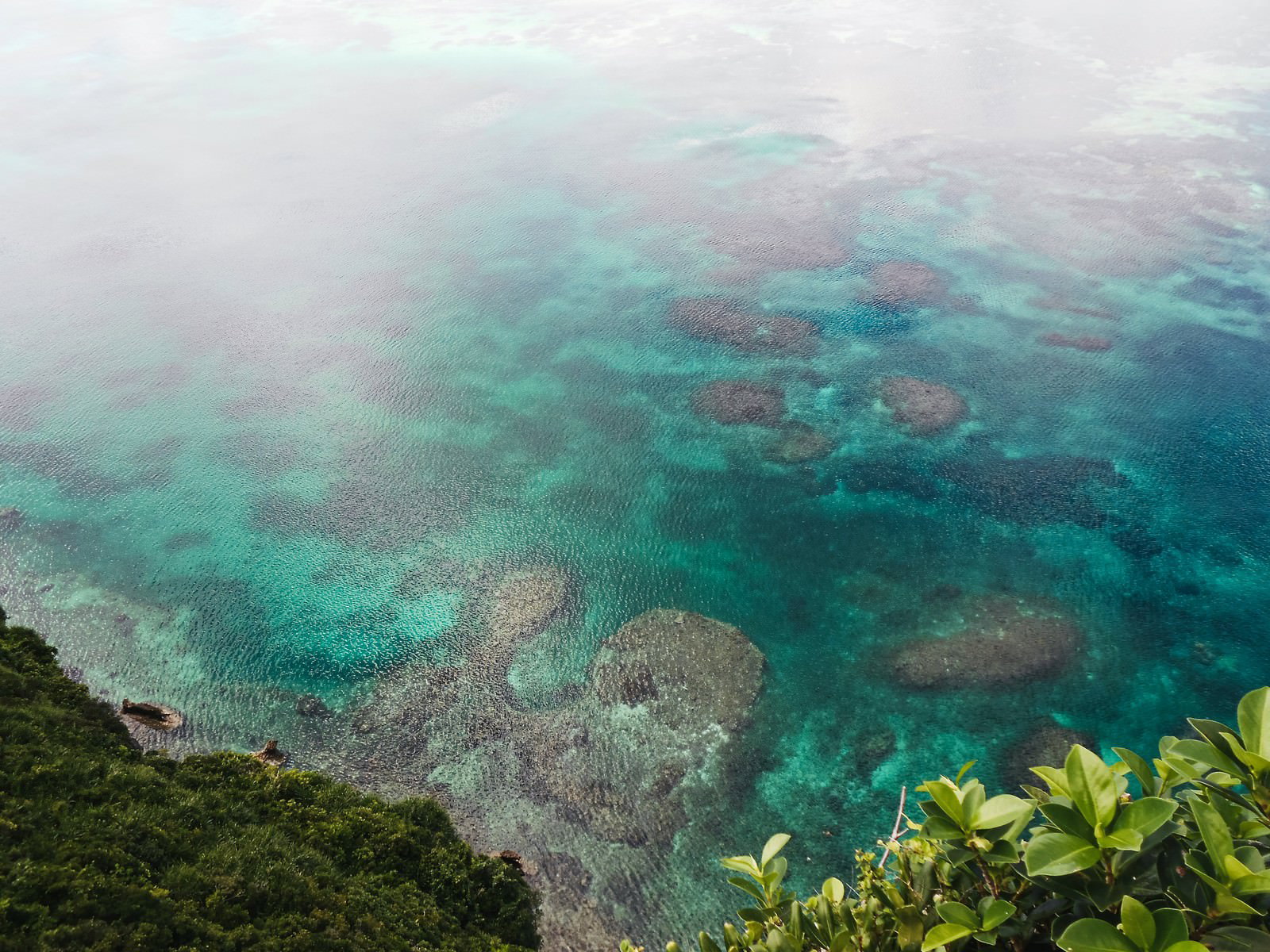 崖上から見下ろすエメラルドグリーンの海岸とサンゴ礁
