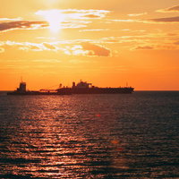 夕焼けに染まるさざ波と船のシルエット、黄昏時の海景の写真