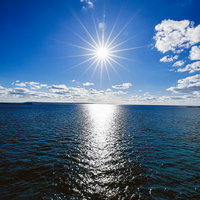 太陽光が海面に輝く青い海と青空、光芒が放つ白い光の道の写真