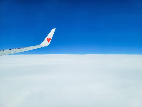 青空と雲海の上を飛ぶ飛行機の翼