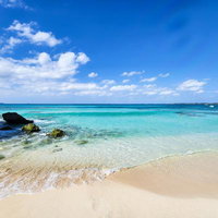 宮古ブルーと白い砂浜に打ち寄せる波と岩場の風景の写真