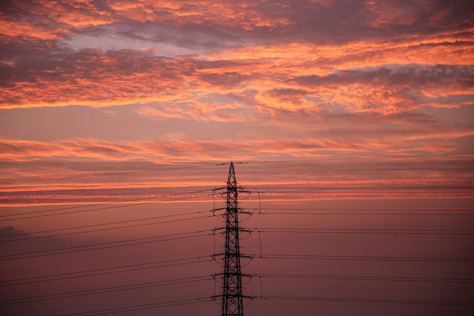 オレンジ色の夕焼け空を背景にシルエット状の鉄塔と送電線