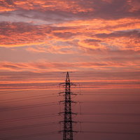 夕焼け空にシルエットの鉄塔と送電線が立ち並ぶ夕暮れ風景の写真
