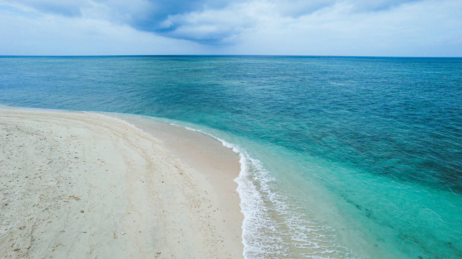 透明度の高いエメラルドグリーンの海と白い砂浜が広がるビーチの風景
