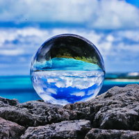 岩場に置かれたガラス玉に映り込む南国リゾートの海と空の写真