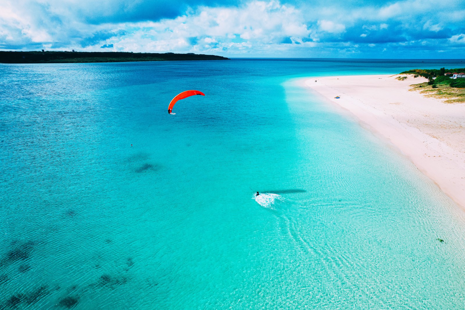 前浜ビーチの白い砂浜とエメラルドグリーンの海でパラセーリングをしている風景