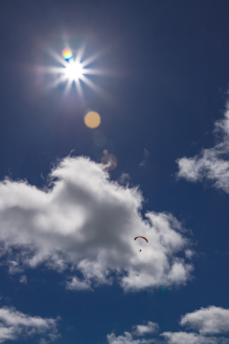 青空を飛ぶパラグライダーと太陽の光芒