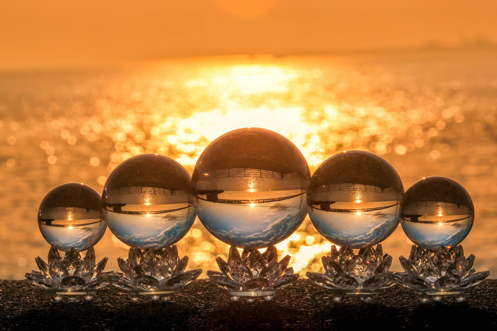 海岸に並ぶ水晶玉と夕日の光芒がオレンジ色に輝く光景