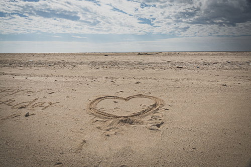 砂浜に描かれたハートと曇り空の海岸風景、波打ち際のロマンチックな恋愛