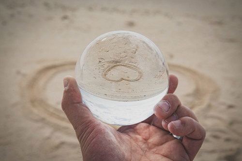 砂浜で手のひらに乗せた水晶玉に映り込む逆ハート