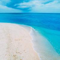 エメラルドグリーンの青い海と波打ち際、白い砂浜の写真