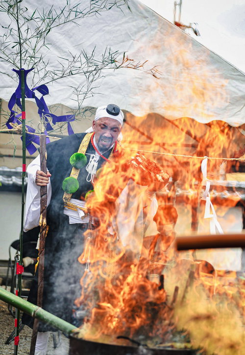 お焚き上げの炎越しに立つ住職