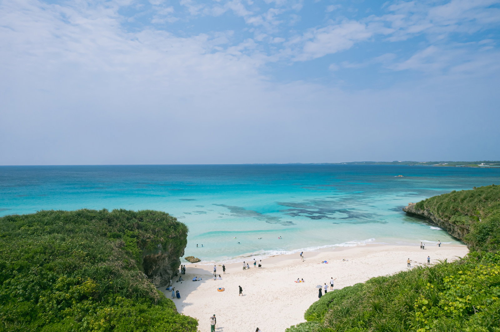 宮古島の砂山ビーチを高台から見下ろした風景。白い砂浜と青い海で泳ぐ人々
