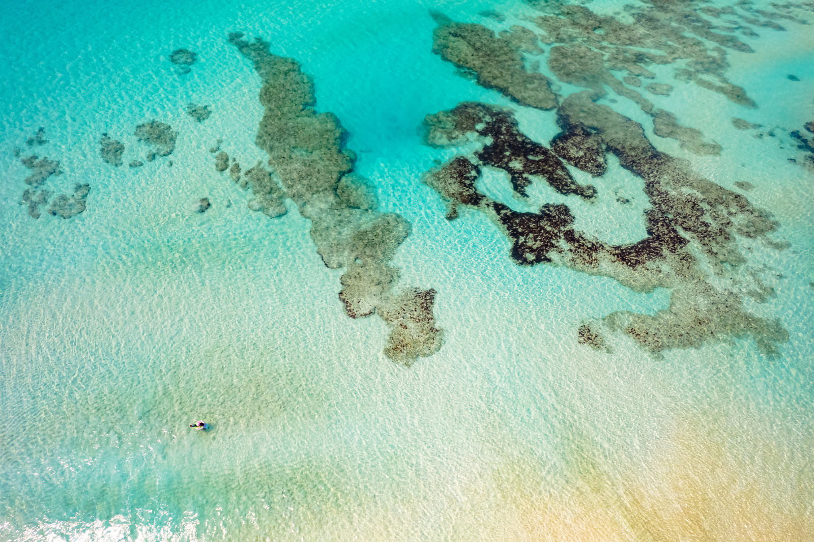 宮古島の透明な海に浮かぶ人とサンゴ礁が見える航空写真