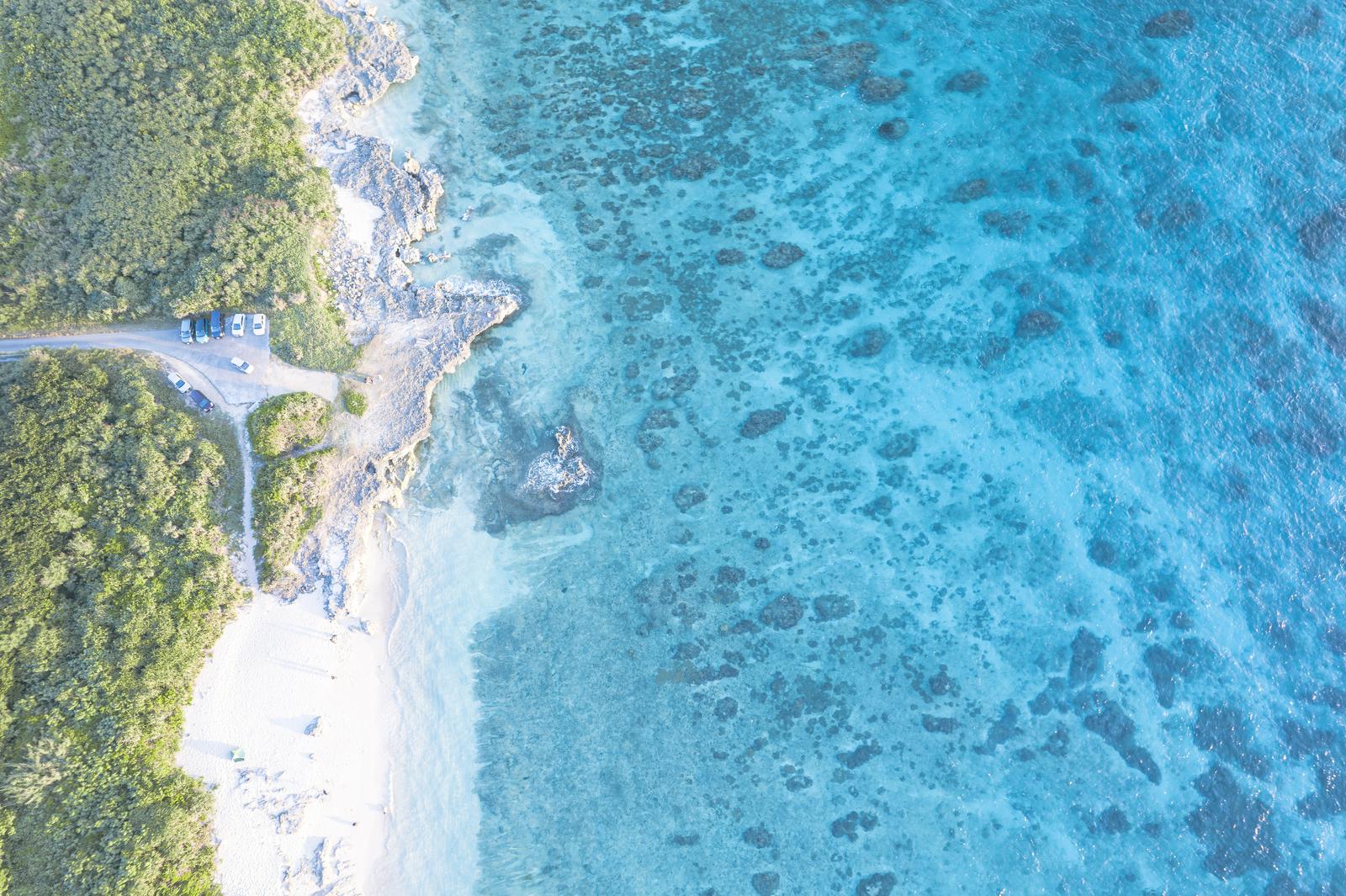 宮古島ムスヌン浜の空撮。白い砂浜と透明な海、樹林帯が見える