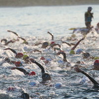 激しく水しぶきを上げるトライアスロン大会の参加者たちの写真