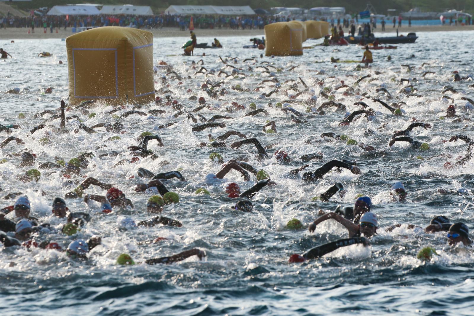 海で一斉にスタートするトライアスロン選手が水しぶきを上げながら泳ぐ様子