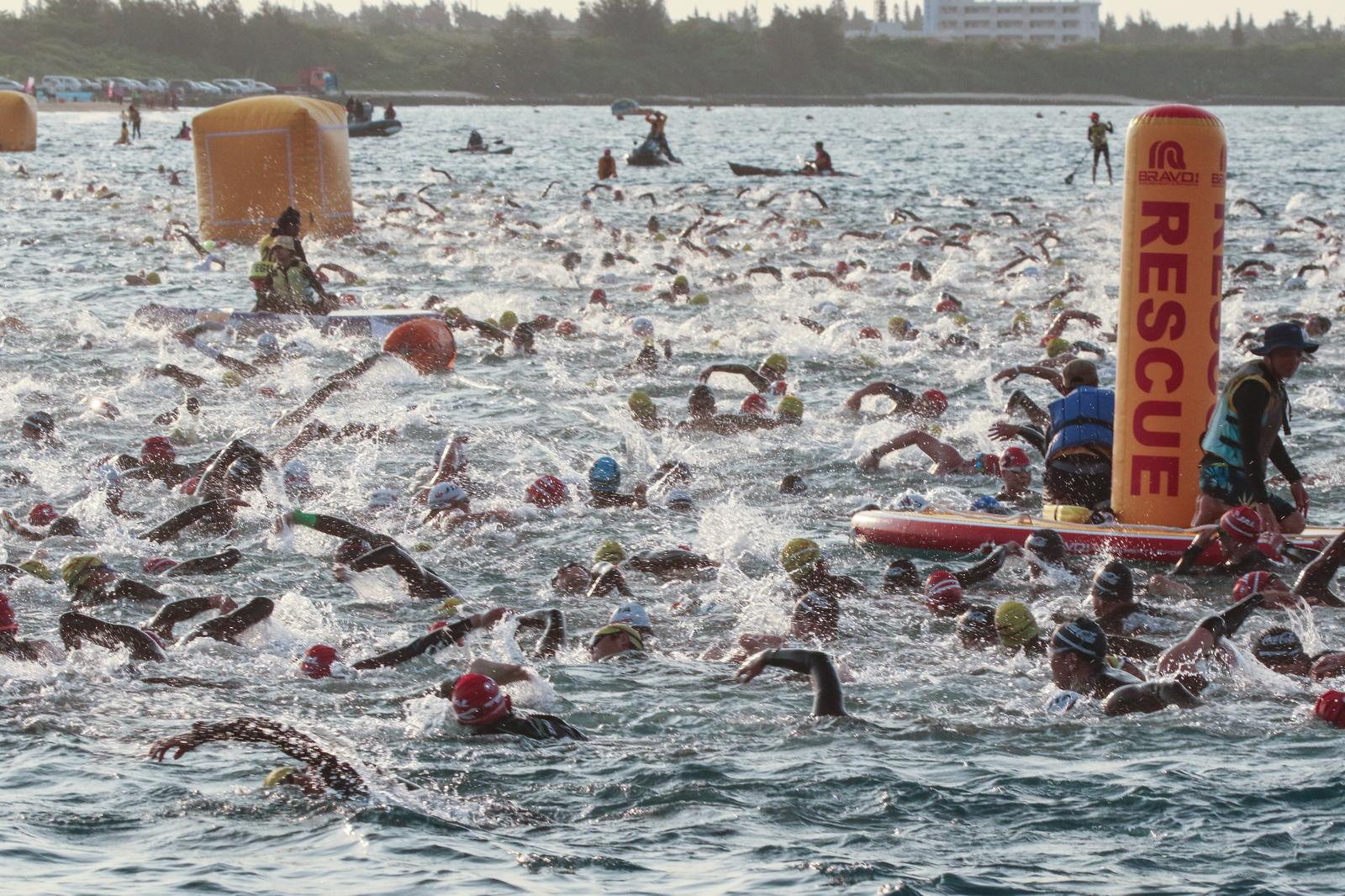 トライアスロンの海でのスイムで水しぶきを上げながら競い合う選手とレスキュー隊員