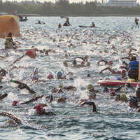トライアスロンの大会で水しぶきを上げながら競い合う選手とレスキュー隊の写真