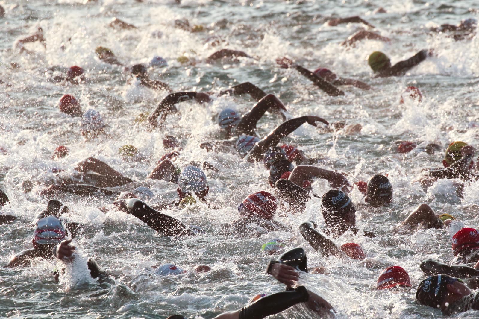 トライアスロンのスイム競技で複数の選手が泳ぎ、激しい水しぶきが立ち上がる様子
