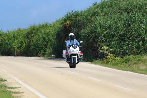 三角点付近の田舎道をパトロールする白バイ