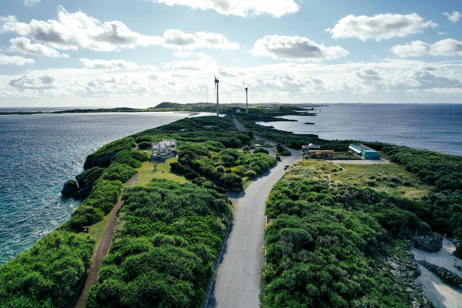 岬の先端に立つ2基の風力発電機と紺碧の海に囲まれた宮古島の景観