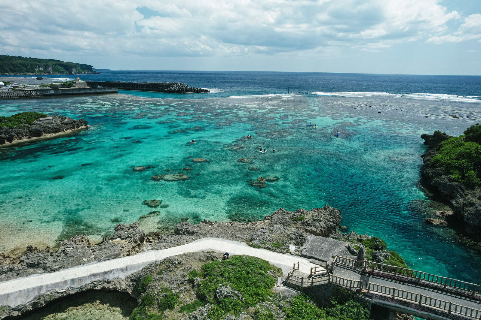 宮古島の岩礁と防波堤から見る透明なエメラルドグリーンの海と遊泳者