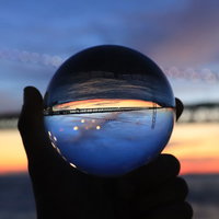 手に持ったガラス玉越しに見た夕焼けと橋のシルエットの写真