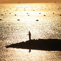 夕焼けにきらめく海で堤防から釣りをするシルエットの写真