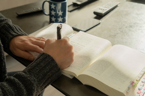 資格試験の勉強中、ペンを握りながら教科書を読む