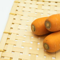 竹ざるの上に並ぶオレンジ色のにんじん2本の写真