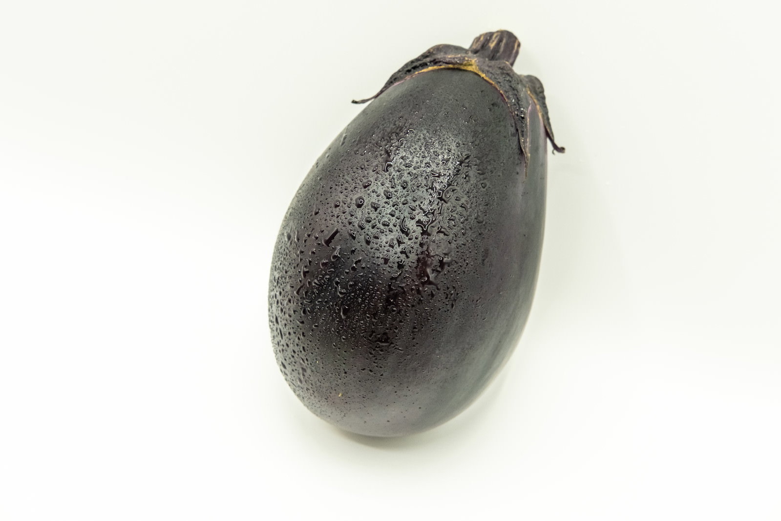 白い背景に置かれた水滴の付いた新鮮な丸ナス