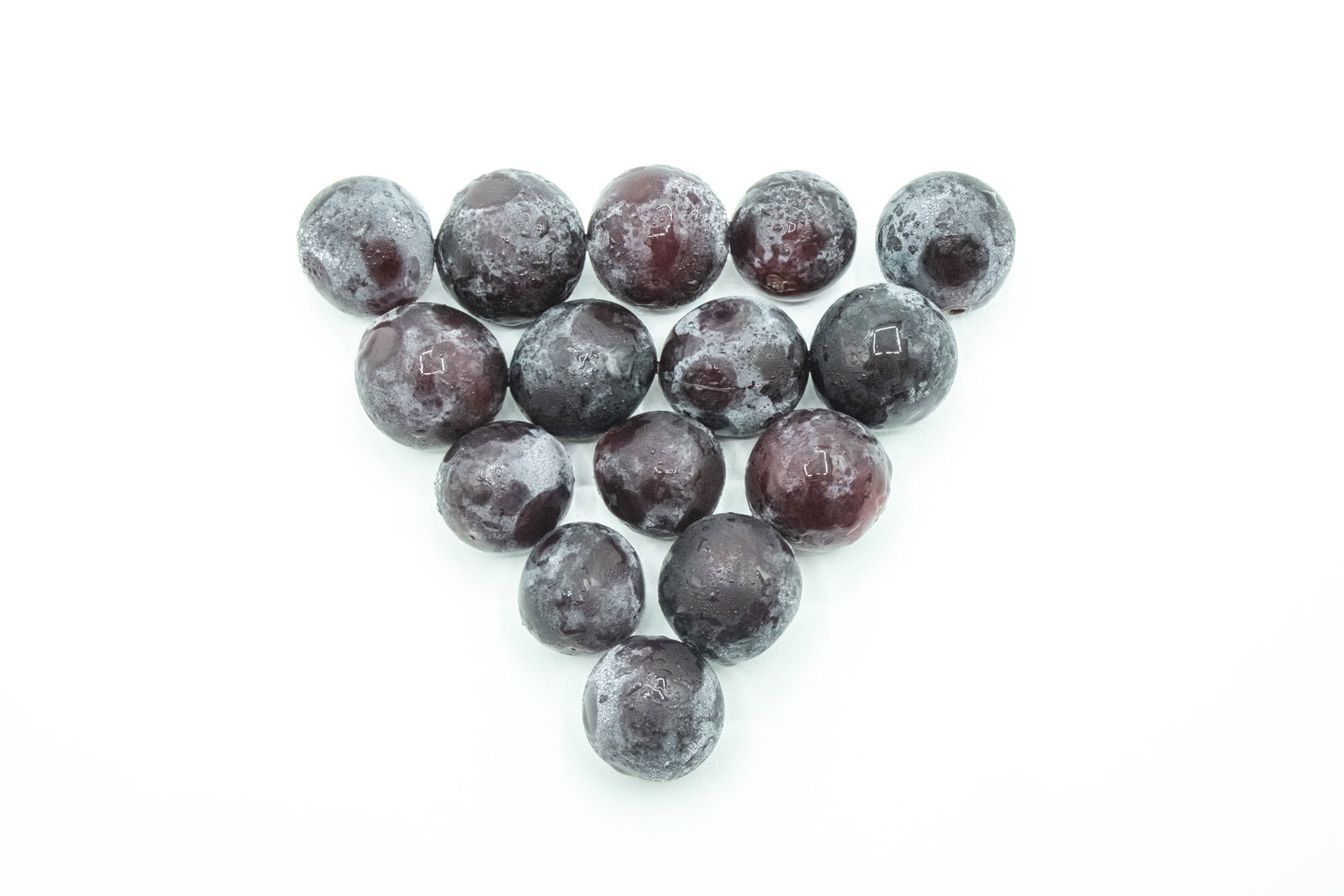 白い背景に三角形に並べられた濃い紫色の種なし巨峰の粒