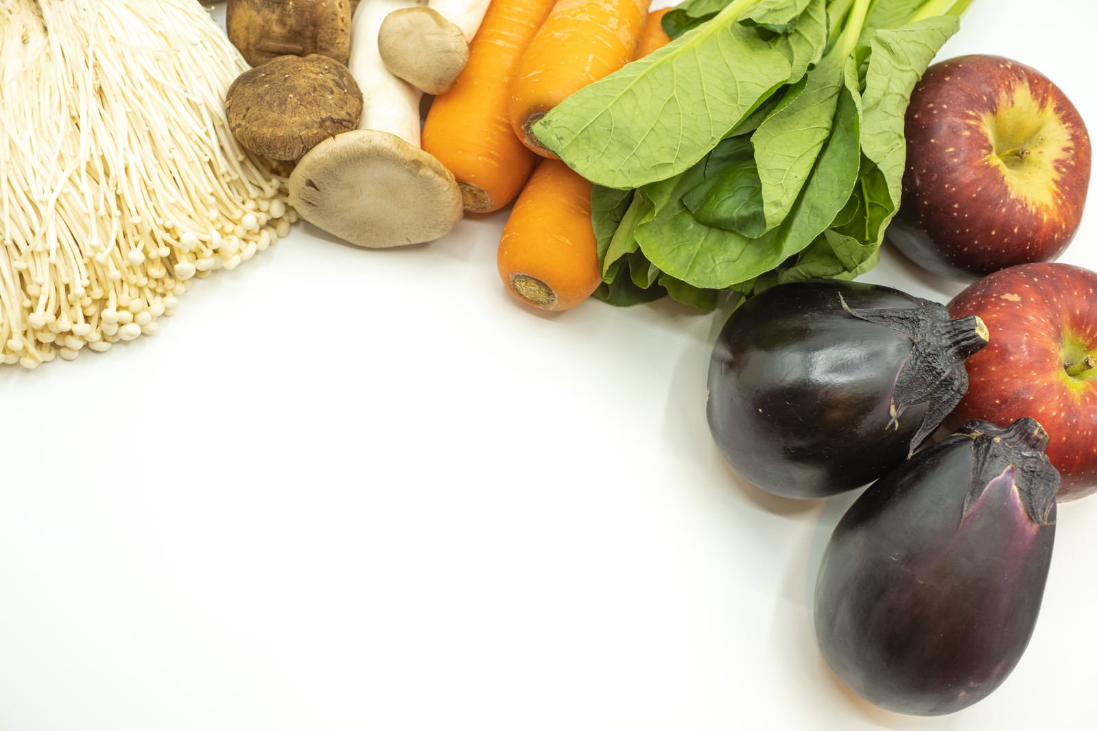 白い背景に人参、茄子、りんご、きのこ類などの新鮮な野菜と果物が並んでいる