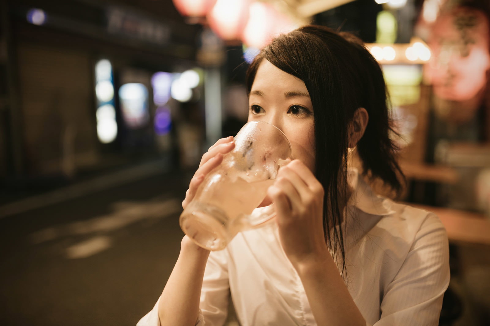 夜の屋外で大きなジョッキを持ってビールを飲む笑顔の女性［モデル：シマヅ］