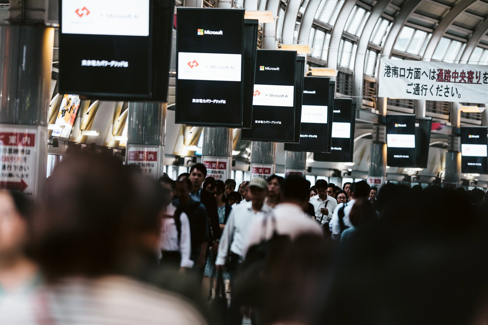 品川駅港南口で電子ディスプレイの下を通行する多くの人々