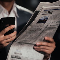 紙面を読んで急いでスマートフォンで検索するビジネスマンの写真