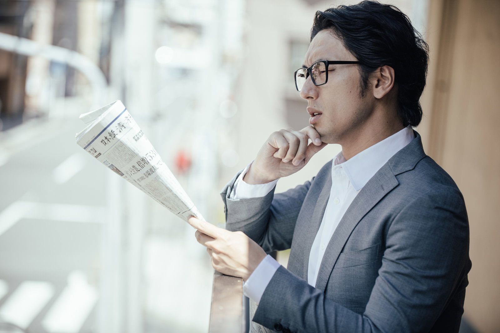 新聞の経済面を真剣に読むスーツ姿の眼鏡をかけたビジネスマン［モデル：大川竜弥］