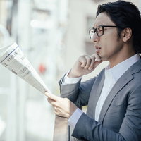 景気の上向きを感じないビジネスマンが新聞を読むの写真