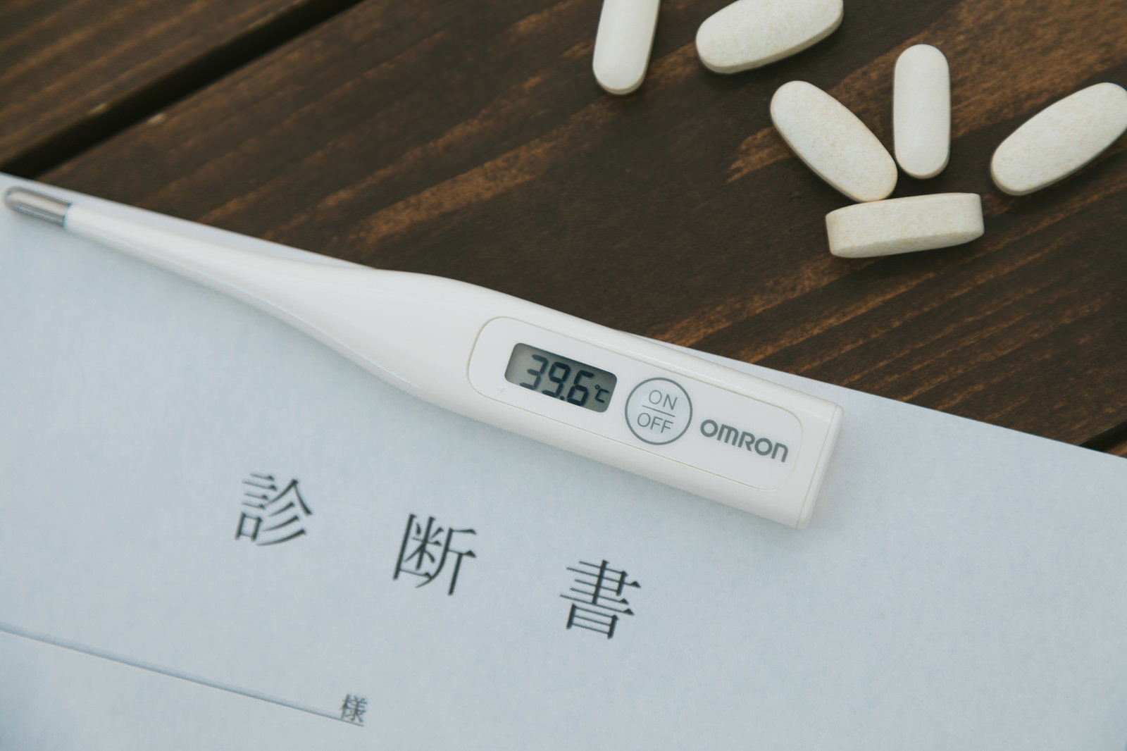 木製テーブルに置かれた診断書と白い錠剤、体温計