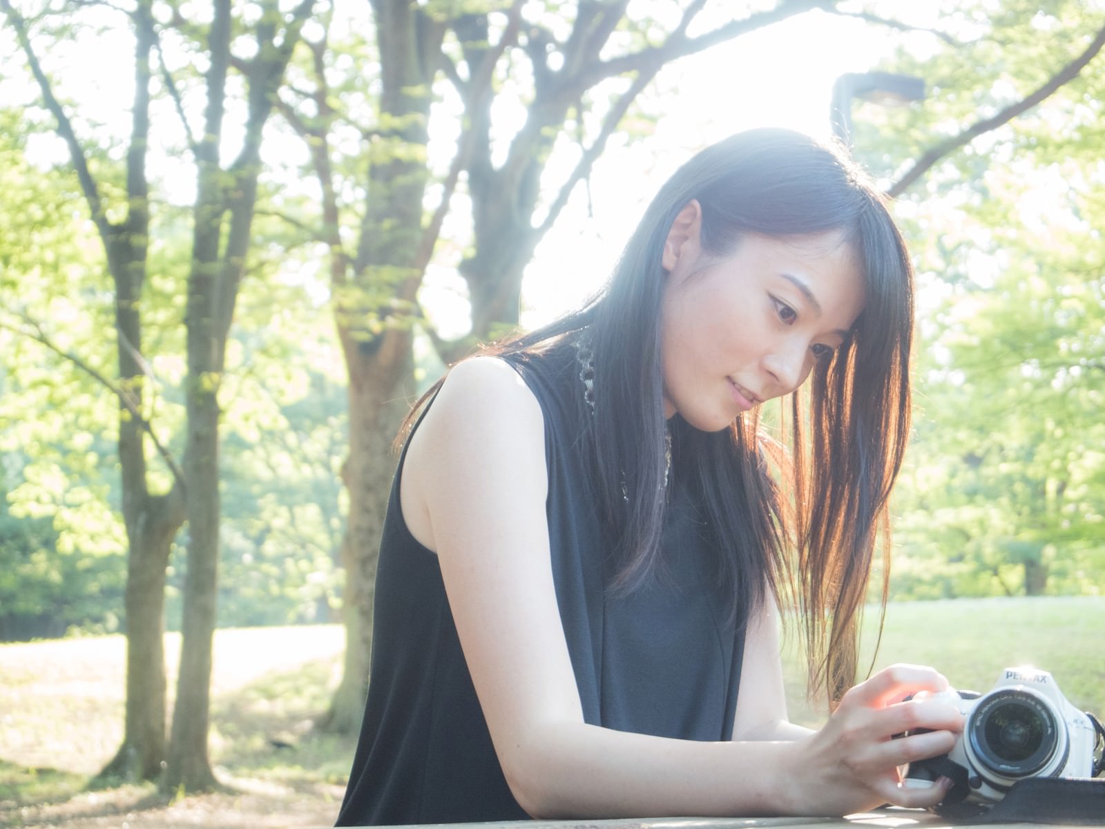 草地でカメラを構える女性［モデル：たけべともこ］
