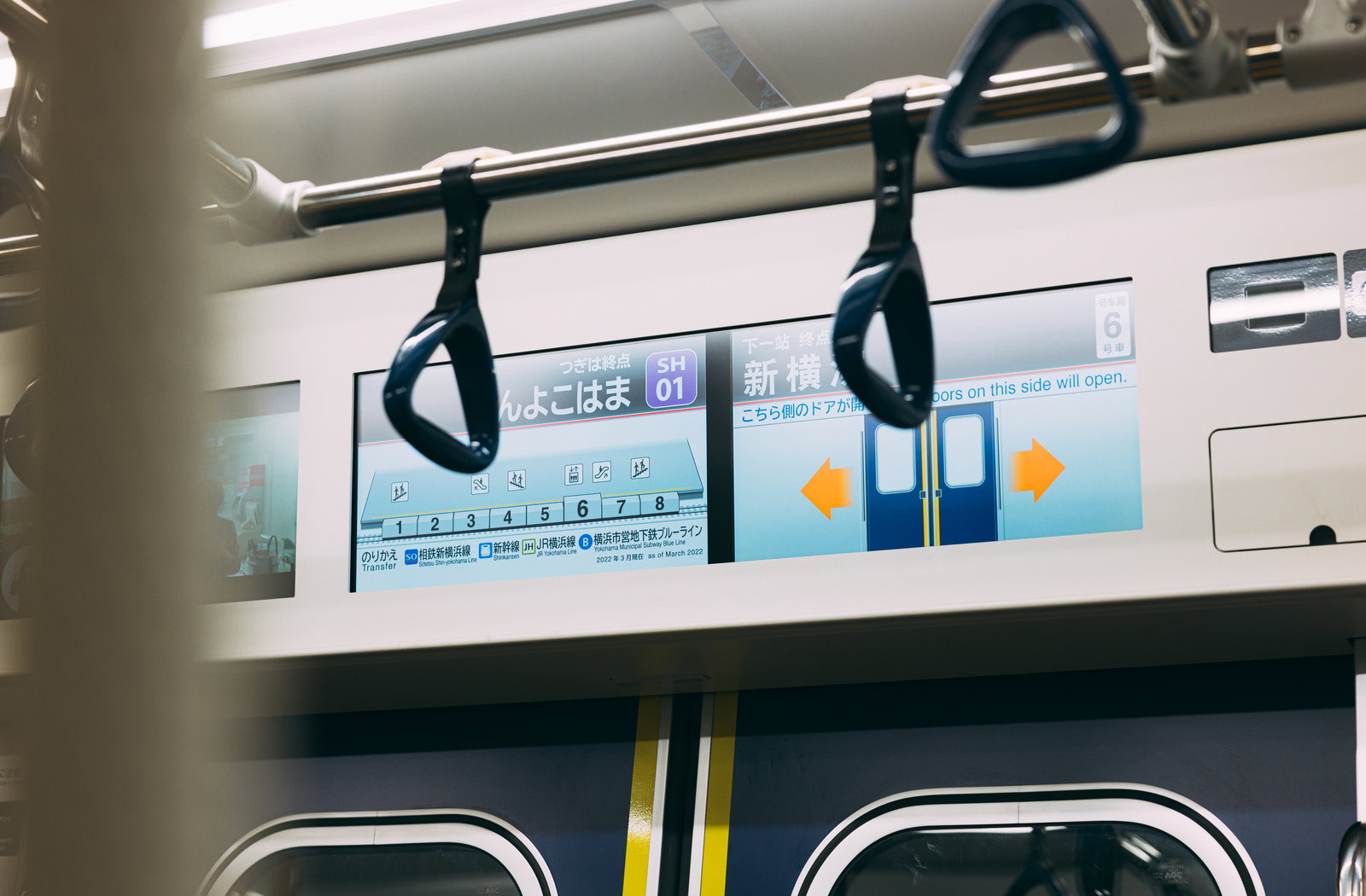 新横浜駅到着を知らせる電車内のつり革と駅案内表示