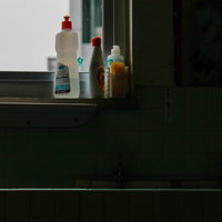 キッチンの手洗い場に並ぶ赤いキャップの洗剤ボトルと洗浄用品の写真