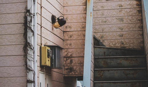 しばらく人が住んでいない廃れたアパートの階段と黄色い公衆電話の写真