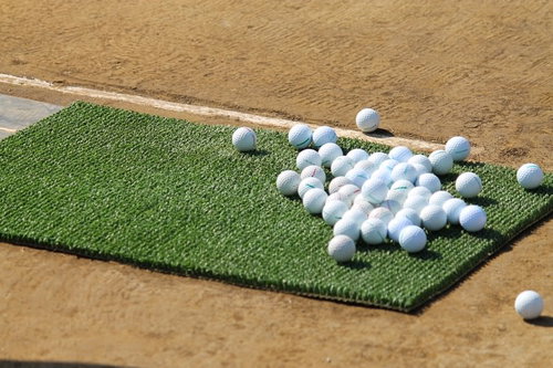 打ちっぱなしの人工芝に並ぶゴルフボールと練習場の風景