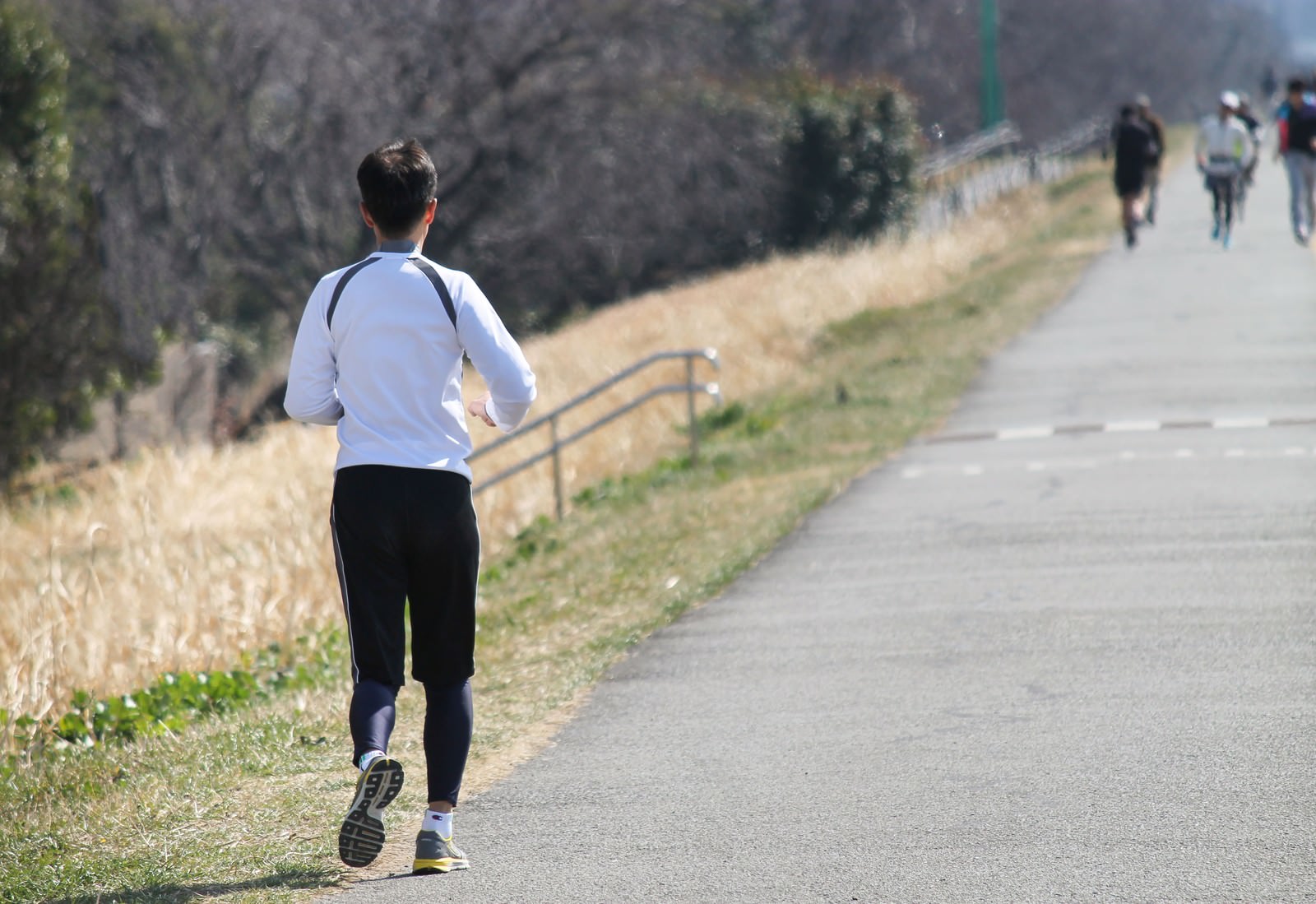 河川敷のランニングコースを走る白いシャツの男性ランナー