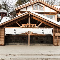 雪が積もる白旗源泉の木造建物、冬の草津温泉の写真