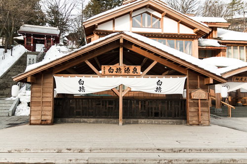 雪が積もる白旗源泉の木造建物、冬の草津温泉