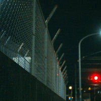 夜間の街灯と信号機が照らすフェンス沿いの道路の写真